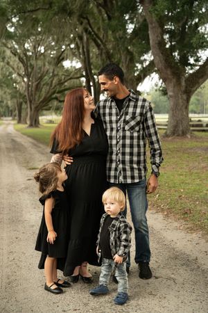 Family walking together on a gravel path surrounded by large oak trees.