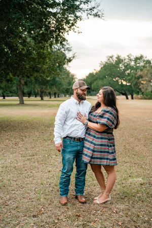 A couple shares a romantic moment together in a park setting with trees in the background.