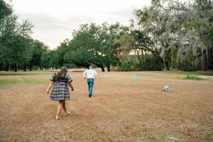 A family plays together in a grassy field surrounded by trees with Spanish moss at dusk.