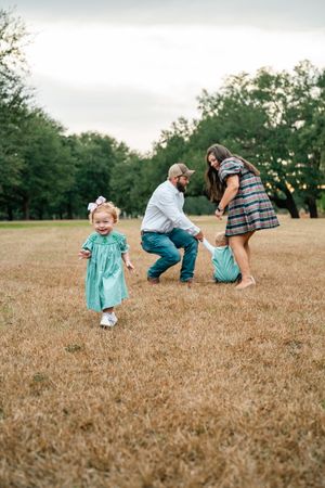 A family plays together in a grassy field with a toddler in a turquoise dress.