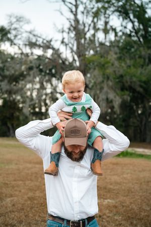 A playful moment captured outdoors with a child riding on shoulders in a natural setting.
