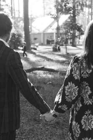A black and white photo shows two people walking through a wooded area, one wearing a floral patterned jacket.