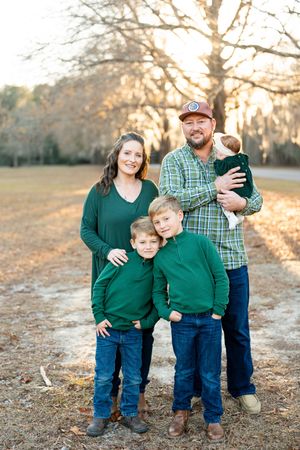 A family wearing coordinated green and blue outfits poses together outdoors during golden hour in autumn.