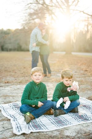 Two children in green sweaters sit together on a blanket during golden hour in a park setting.