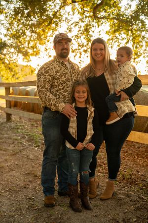 Family photo session outdoors with fall foliage and wooden fence in background.