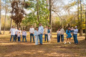 A group of people in coordinating blue and white outfits gather together in a sunlit wooded area during autumn.