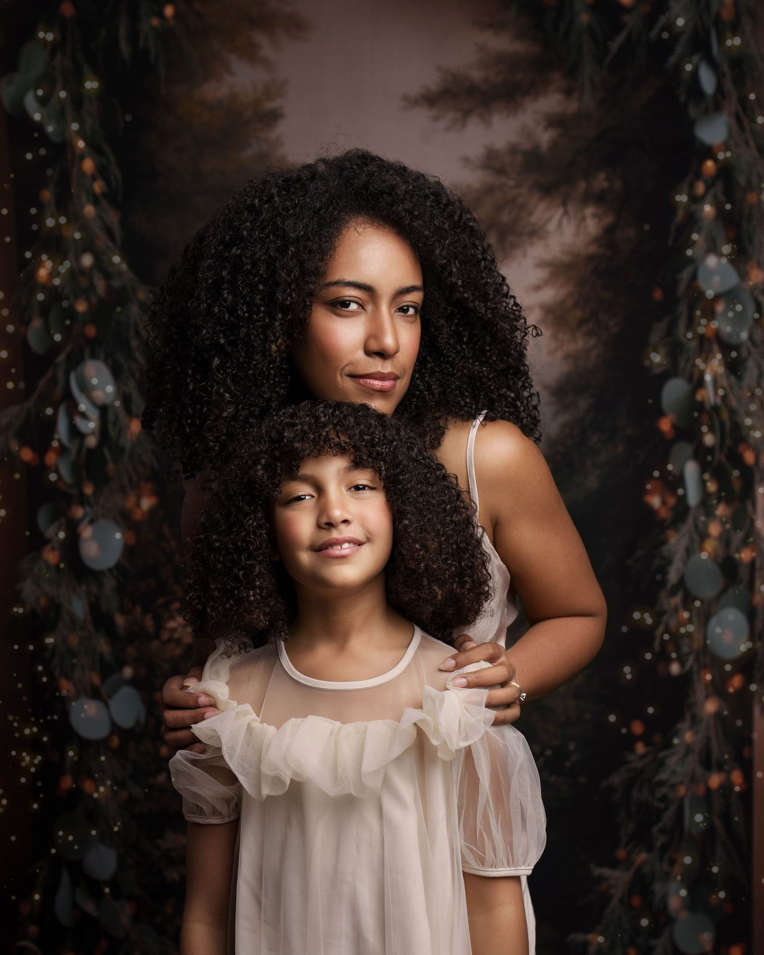 A child with natural curly hair wearing a white dress poses against a dark moody background with twinkling lights.