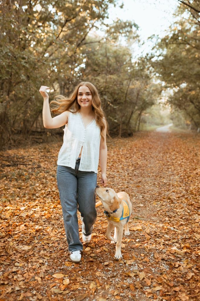 A person and their yellow Labrador puppy playing together on a path covered in fallen autumn leaves.