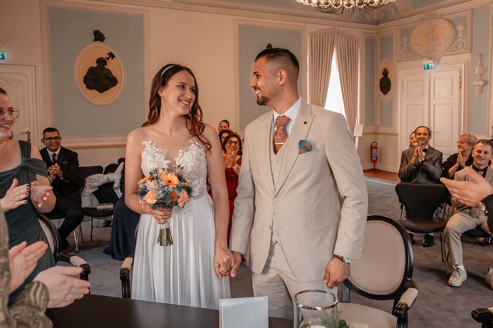 Wedding party celebrates in an elegant ballroom with crystal chandelier and white decor.