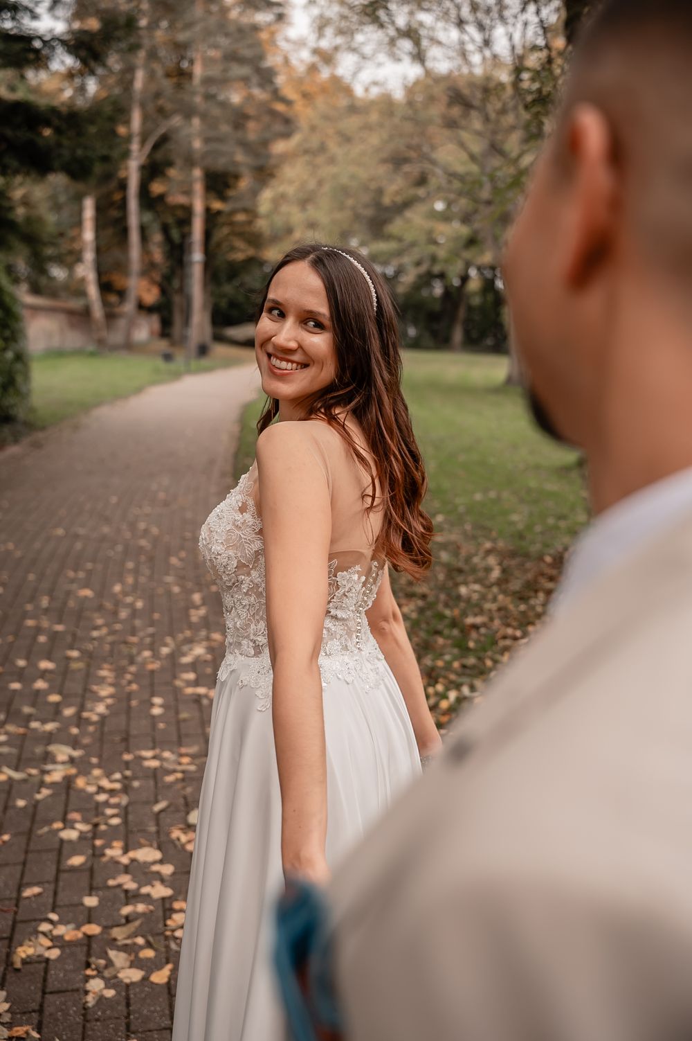 Romantic autumn wedding photoshoot on a tree-lined path covered in fallen leaves.
