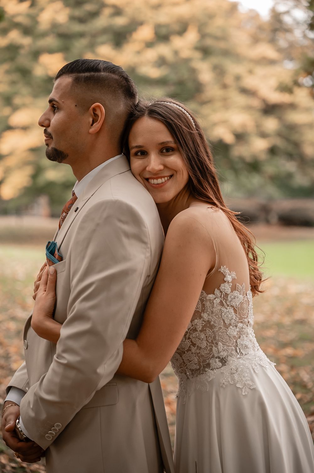 A romantic outdoor wedding photoshoot with a couple in beige and white attire against a sunset backdrop.