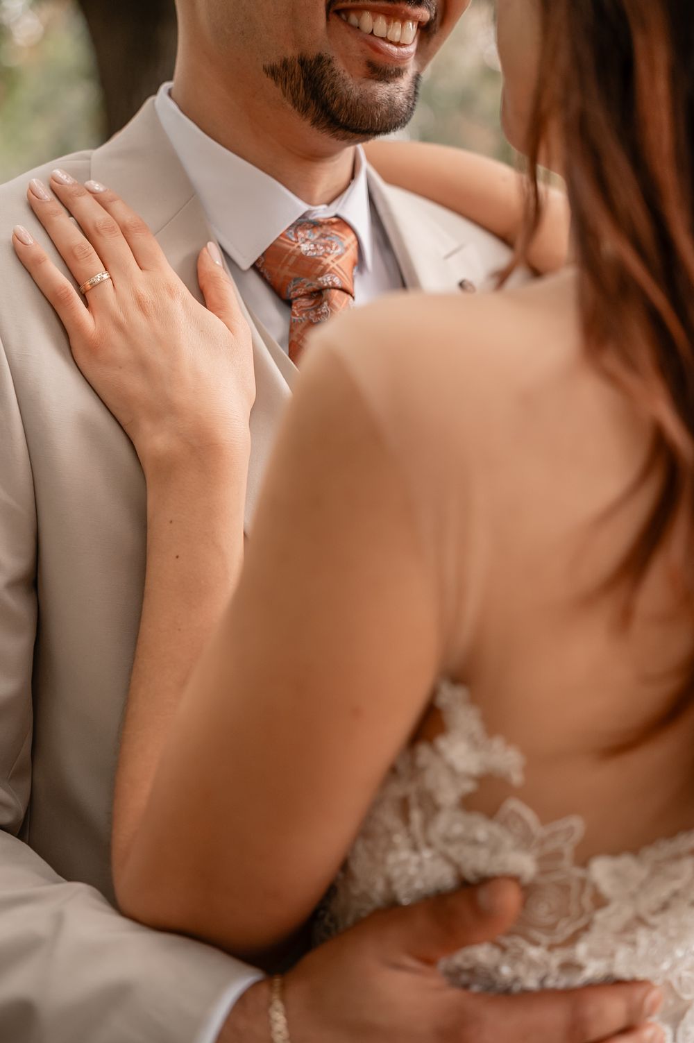 Close-up shot of a bride and groom embracing during their wedding, with focus on her hand resting on his shoulder.