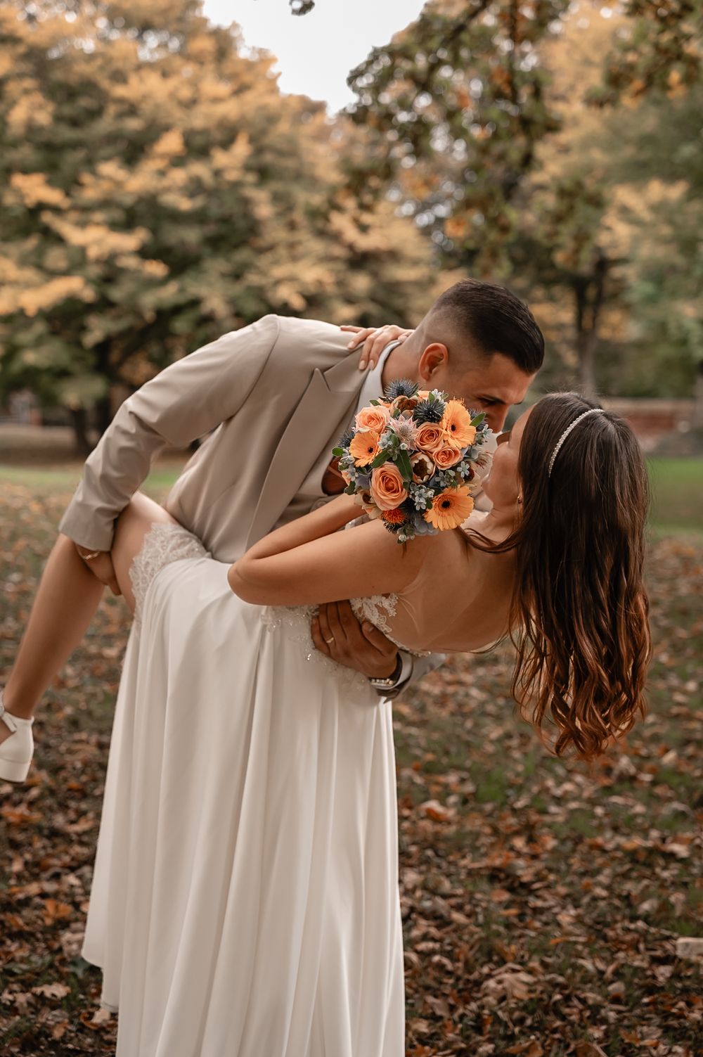 A playful wedding couple dips low during an autumn photoshoot surrounded by fallen leaves.
