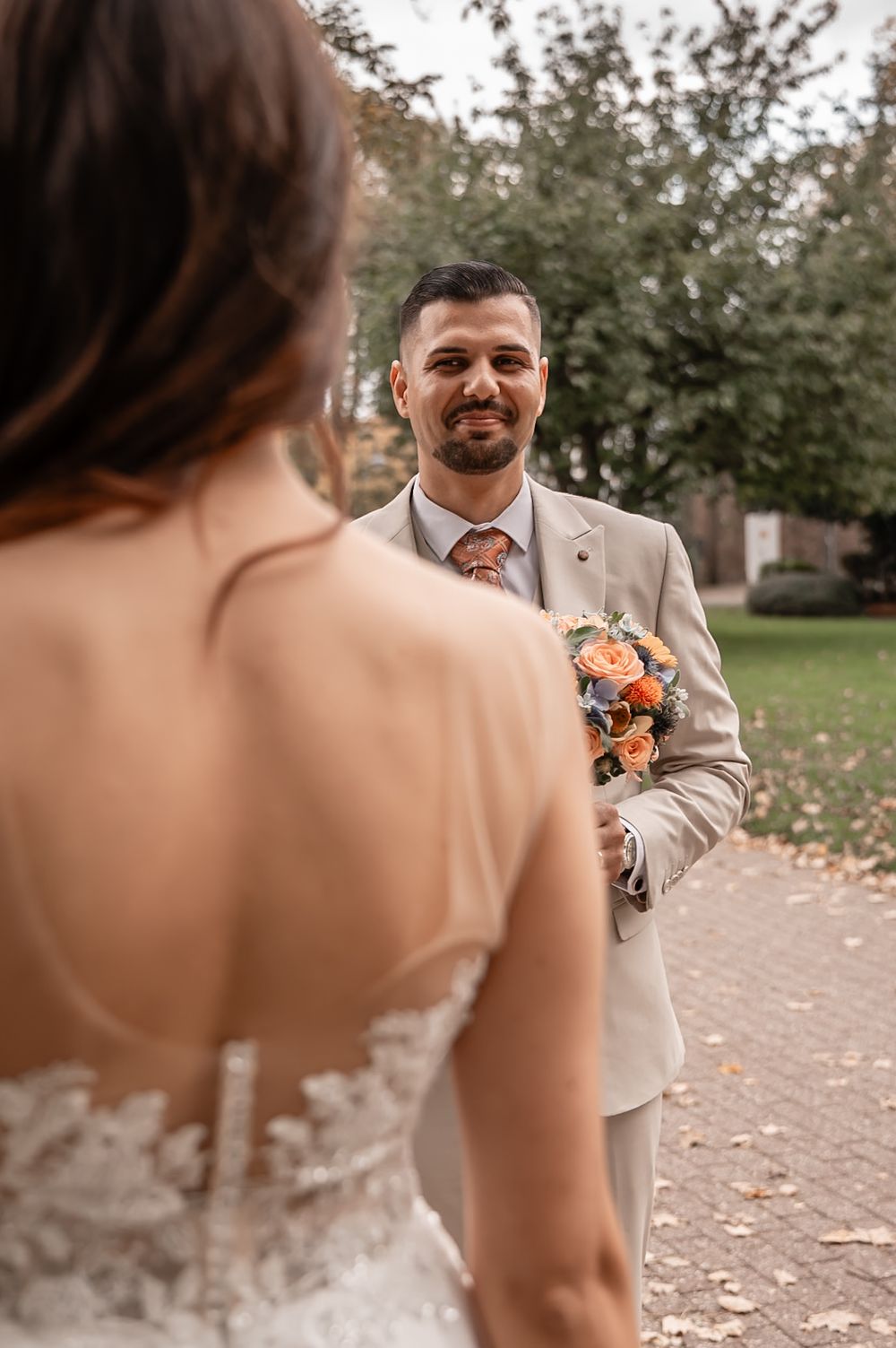 Wedding couple shares first look moment on brick pathway surrounded by fall foliage.