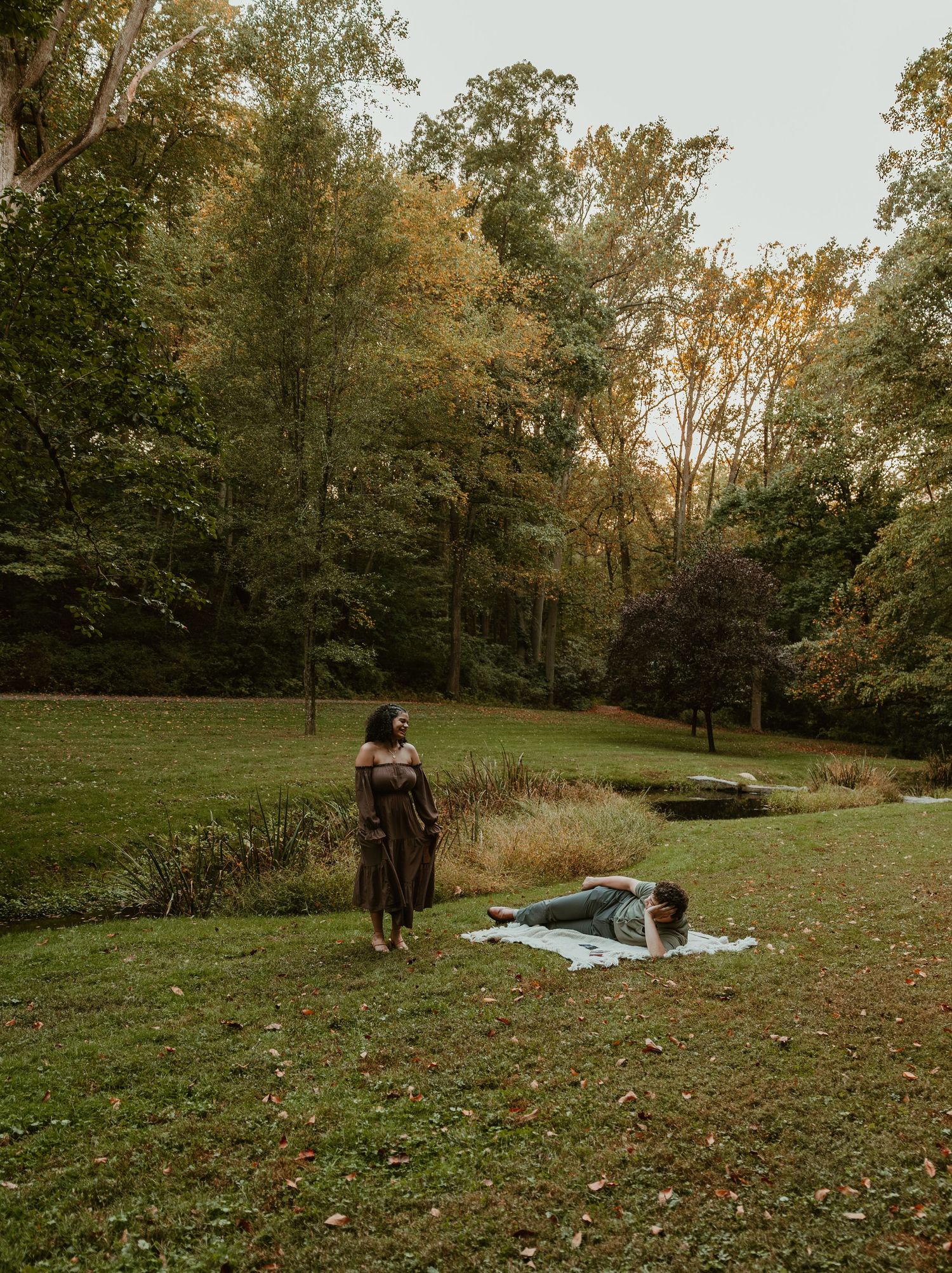 A peaceful autumn scene in a park with a picnic blanket laid out on grass surrounded by golden-leaved trees.