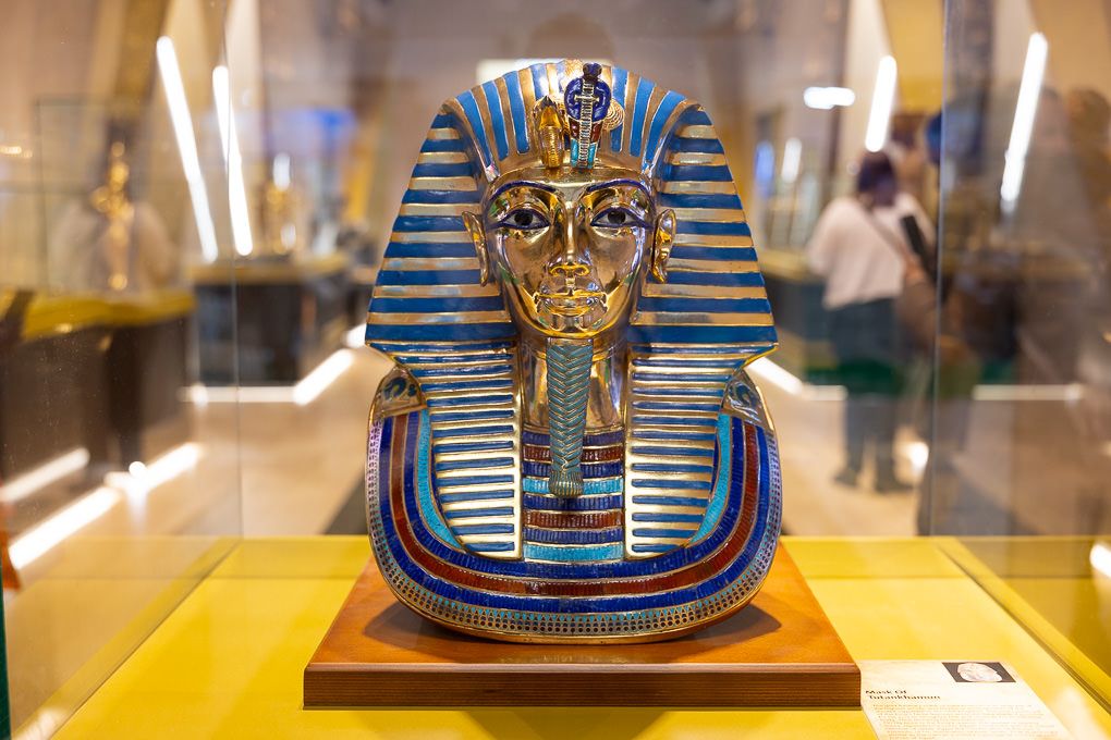 A golden King Tutankhamun death mask displayed in a museum exhibit case at the 2025 WTM in the ExCel, London.