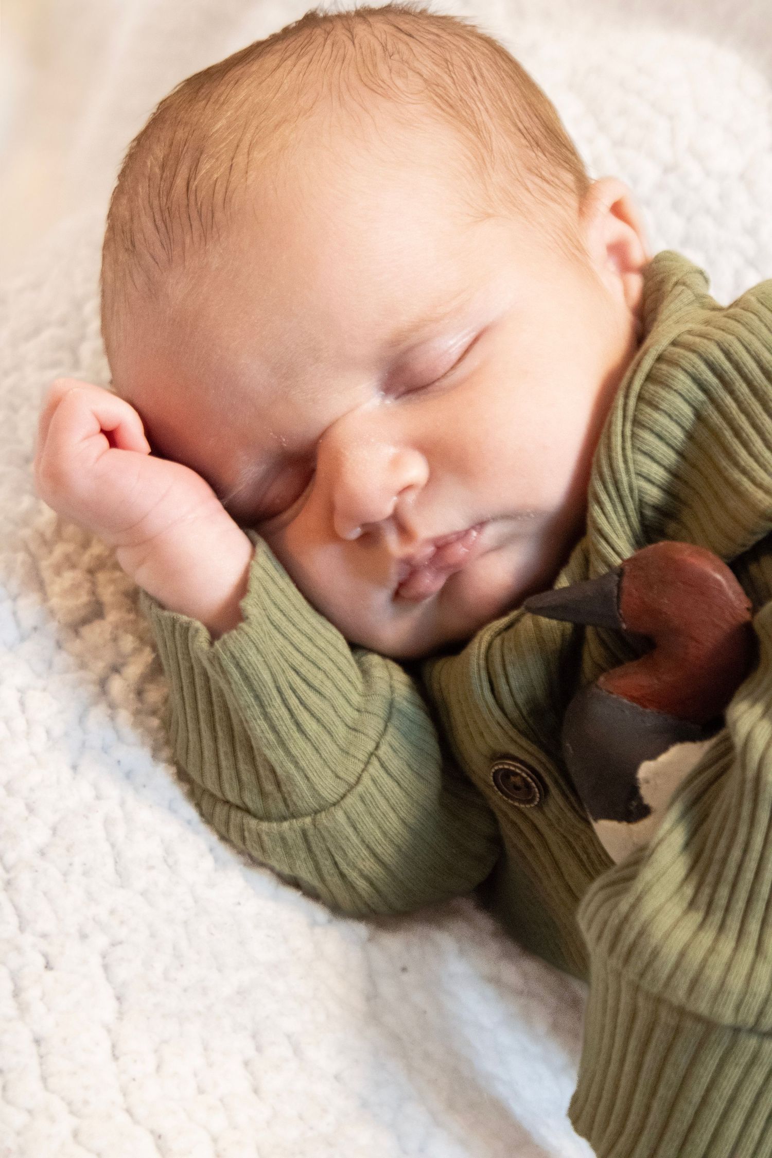 A sleeping baby in a green sweater lies peacefully on soft white bedding.