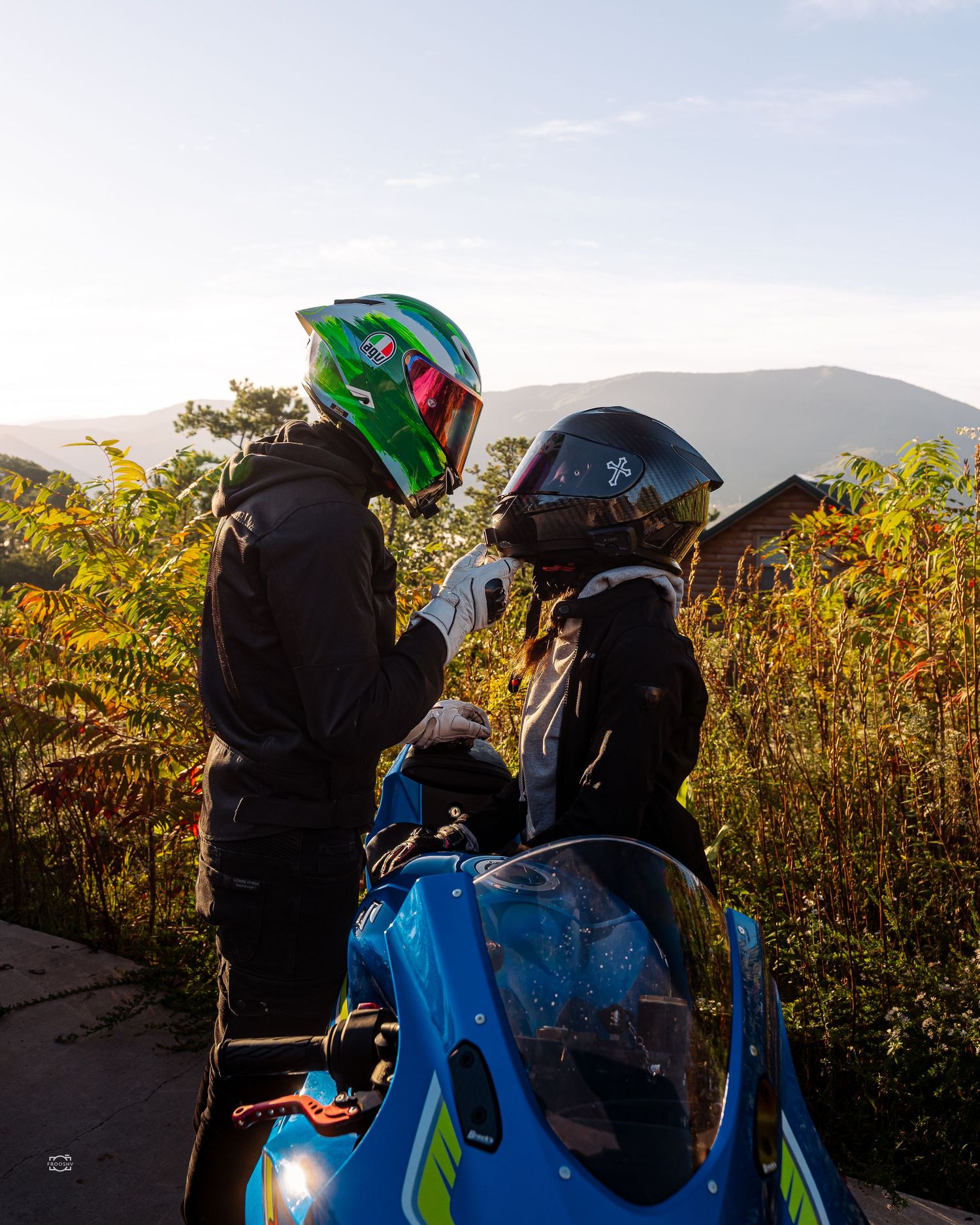 Group of motorcyclists with helmets gathered near sunflower field during golden hour.