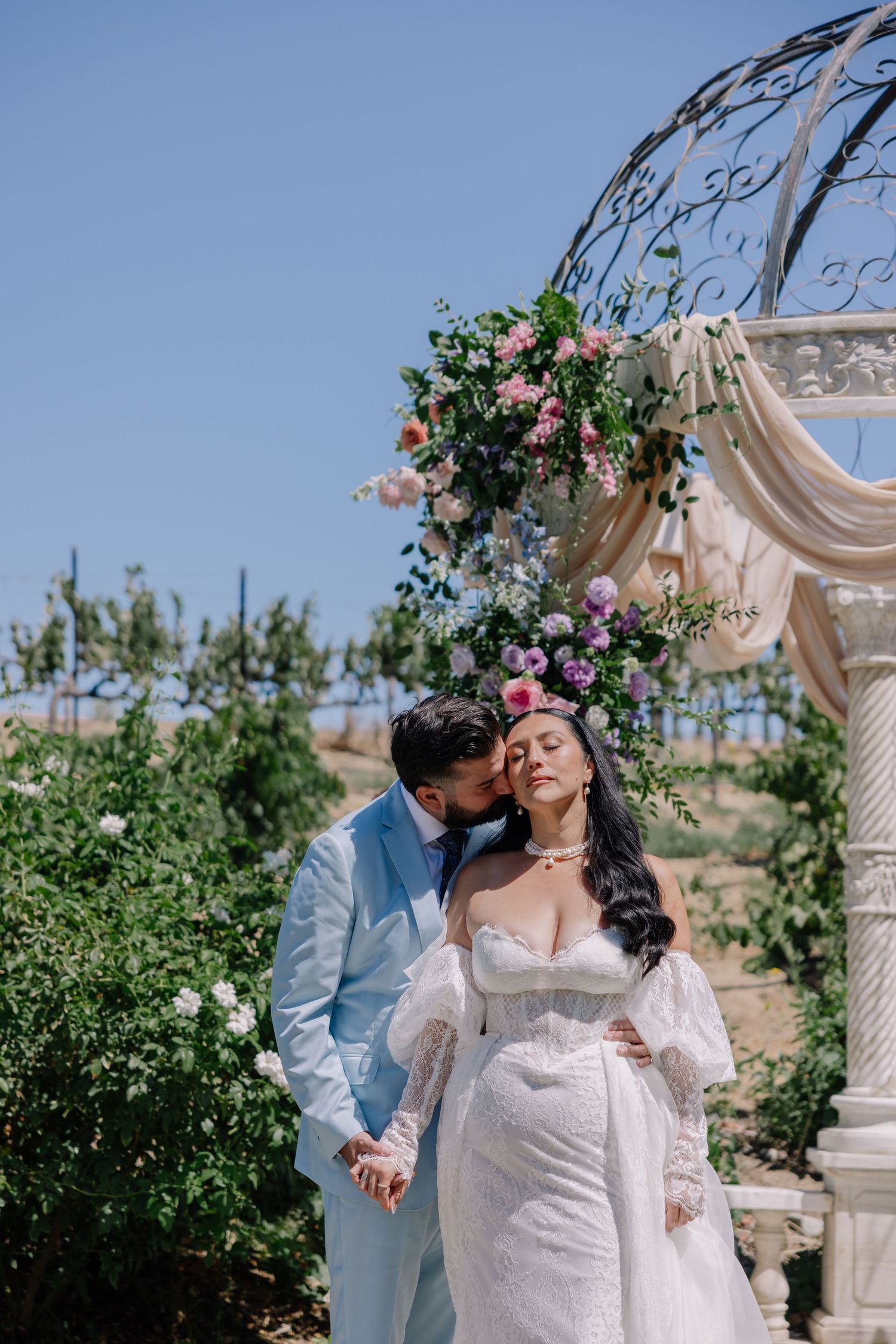Wedding ceremony in garden setting with floral arch and greenery.