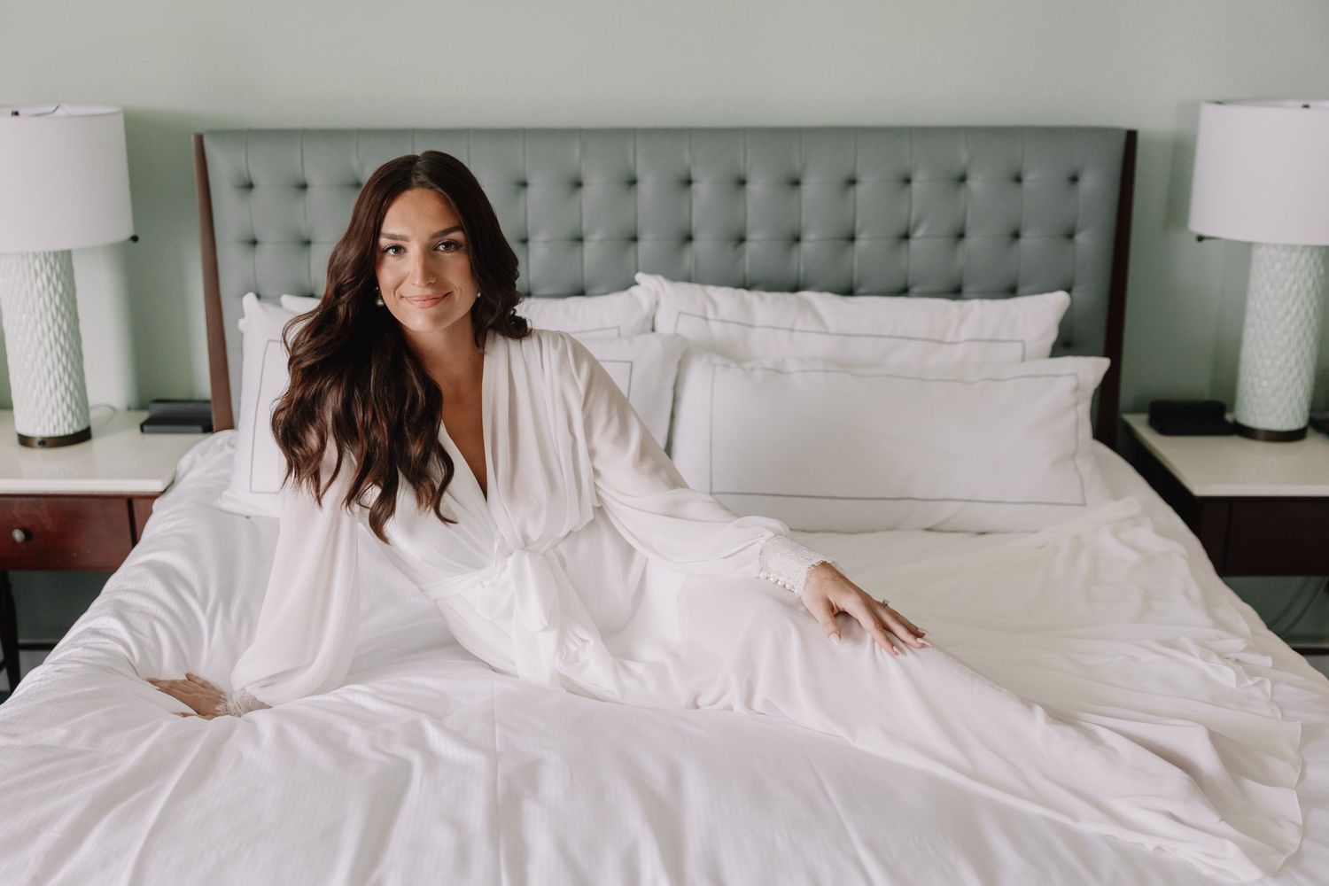 Friends lounging and laughing together on large white hotel bed.