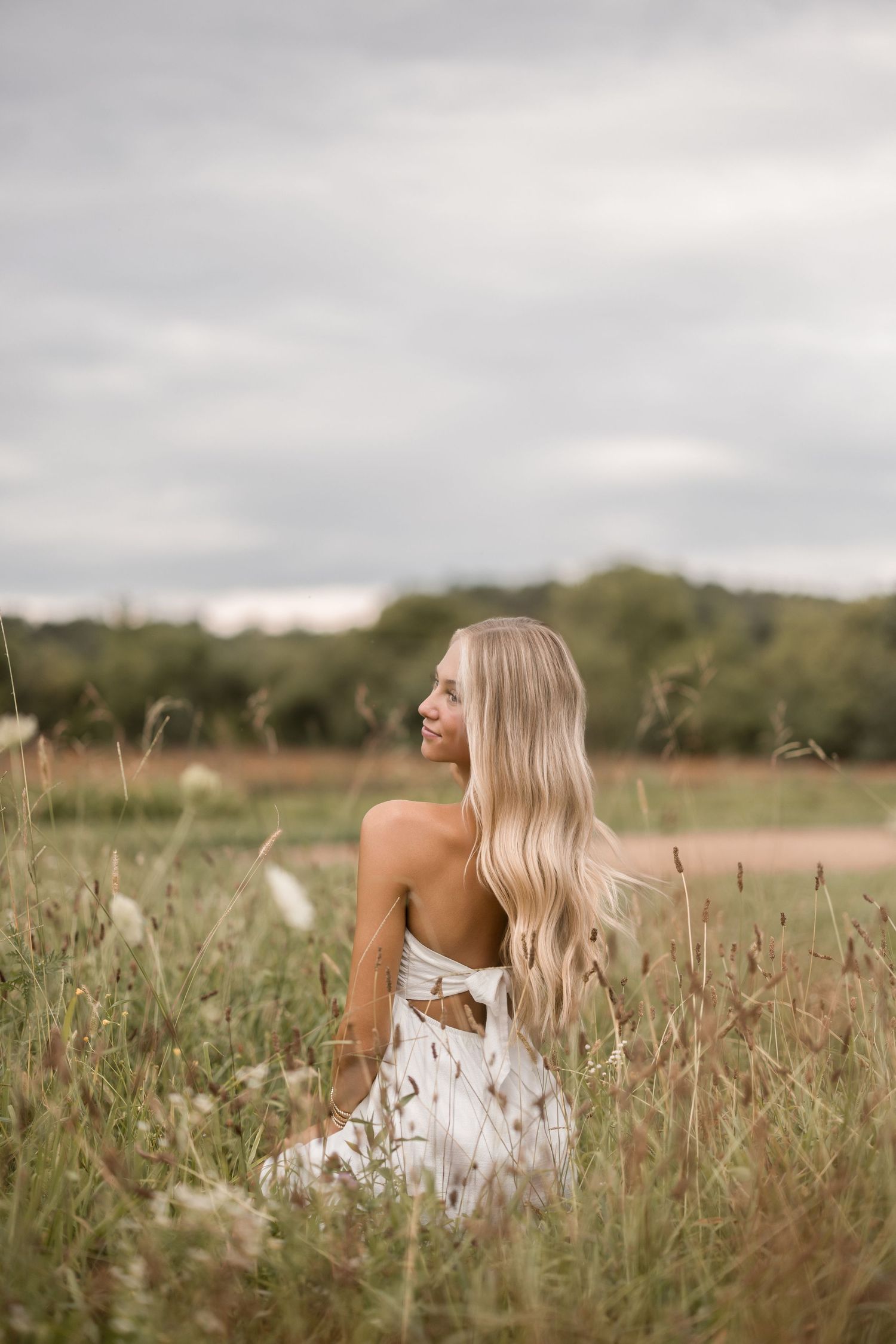 A woman in a white dress sits peacefully among tall grass in a serene field during golden hour.