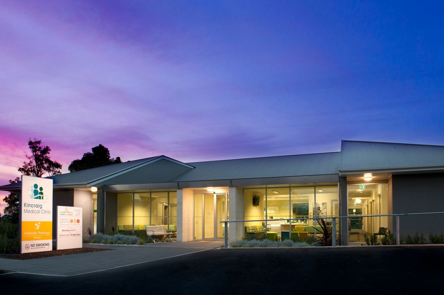 Modern medical facility exterior at sunset with illuminated windows and signage.
