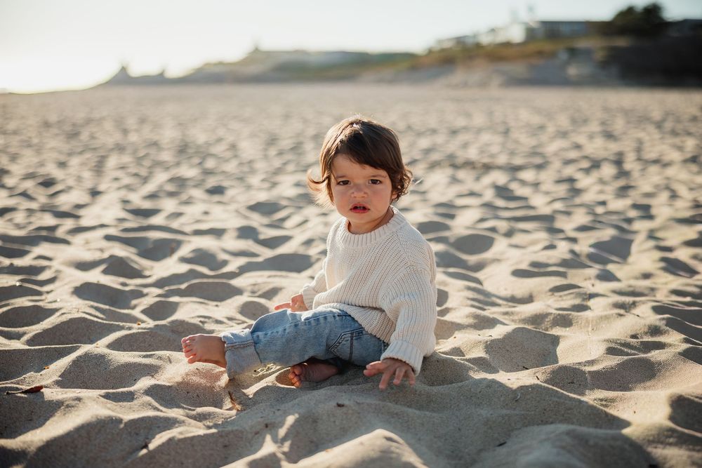 A series of beach photos showing a small child playing in the soft sand during a sunny day.