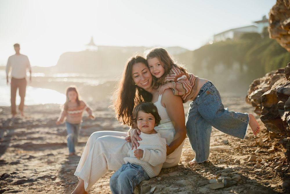 A family enjoys a sunset photoshoot together on a rocky beach with golden light filtering through the scene.