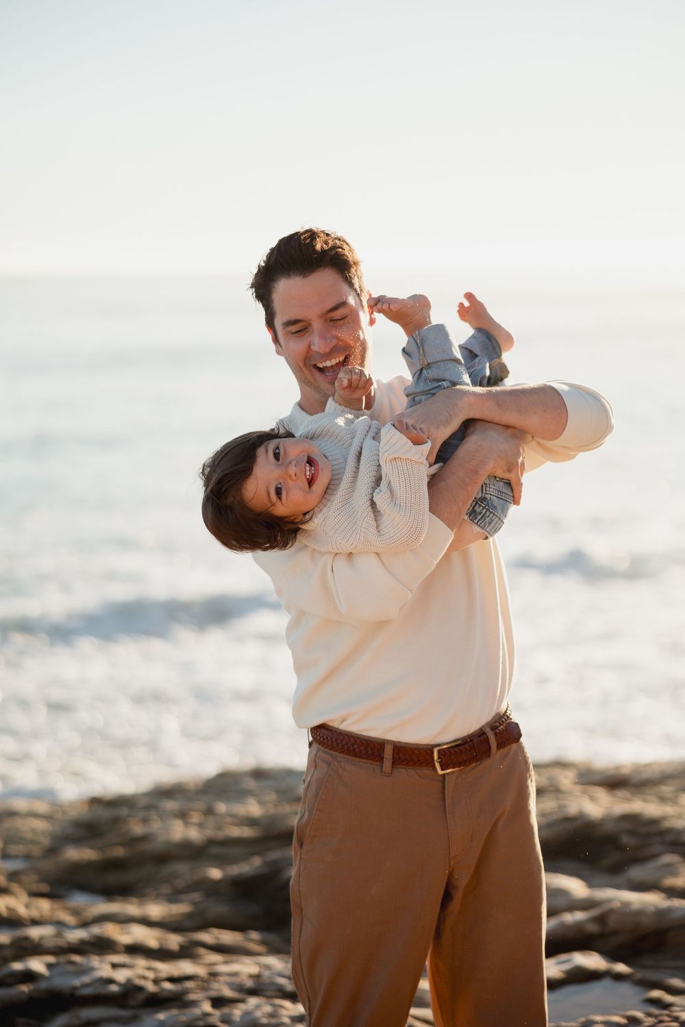 Playful couple poses on rocky beach during sunset photoshoot.