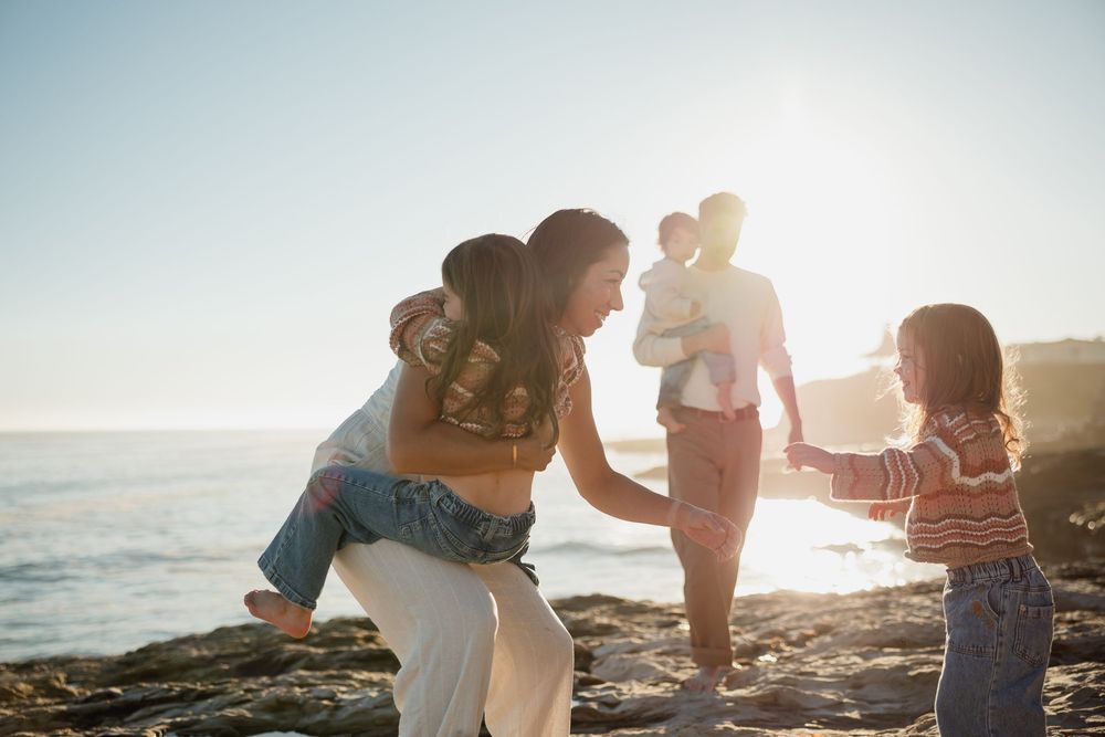 Family walking together along rocky beach coastline during golden hour sunset.