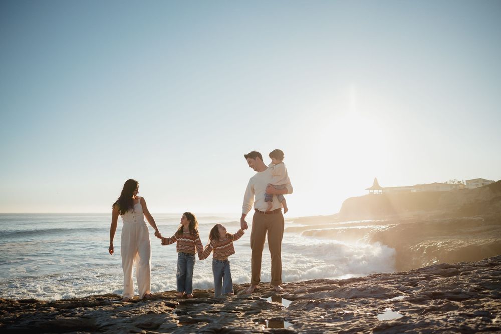 Silhouettes of family holding hands while walking along beach shoreline at dusk.