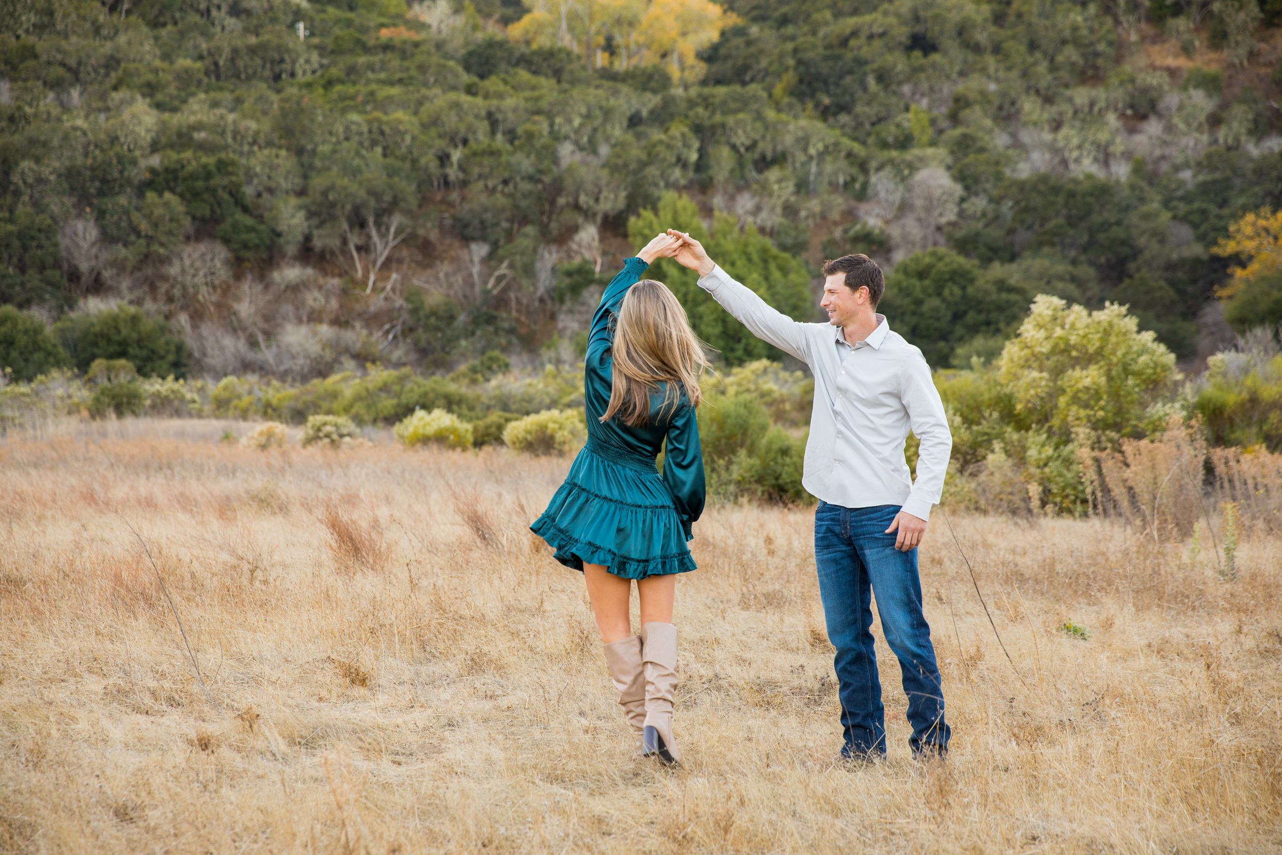 A couple dances together in a golden field with mountains and brush in the background in Carmel Valley, CA.