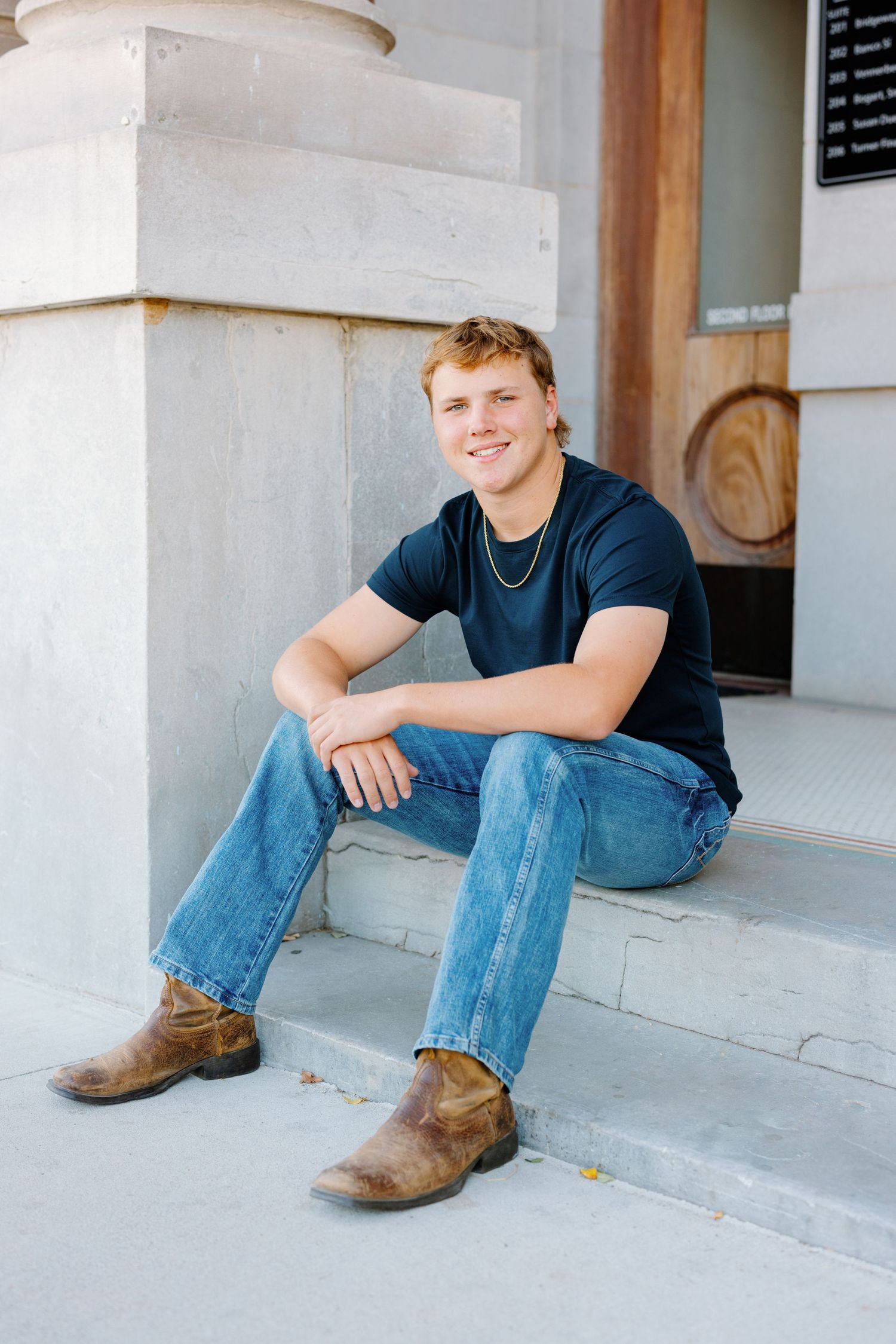 A casual portrait of someone sitting on concrete steps wearing jeans and boots.
