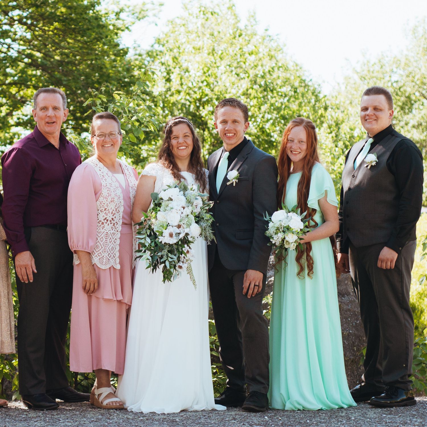 A newly married couple stand smiling with their parents and siblings by their side in Olean, NY. Captured by M. Rose Photography.
