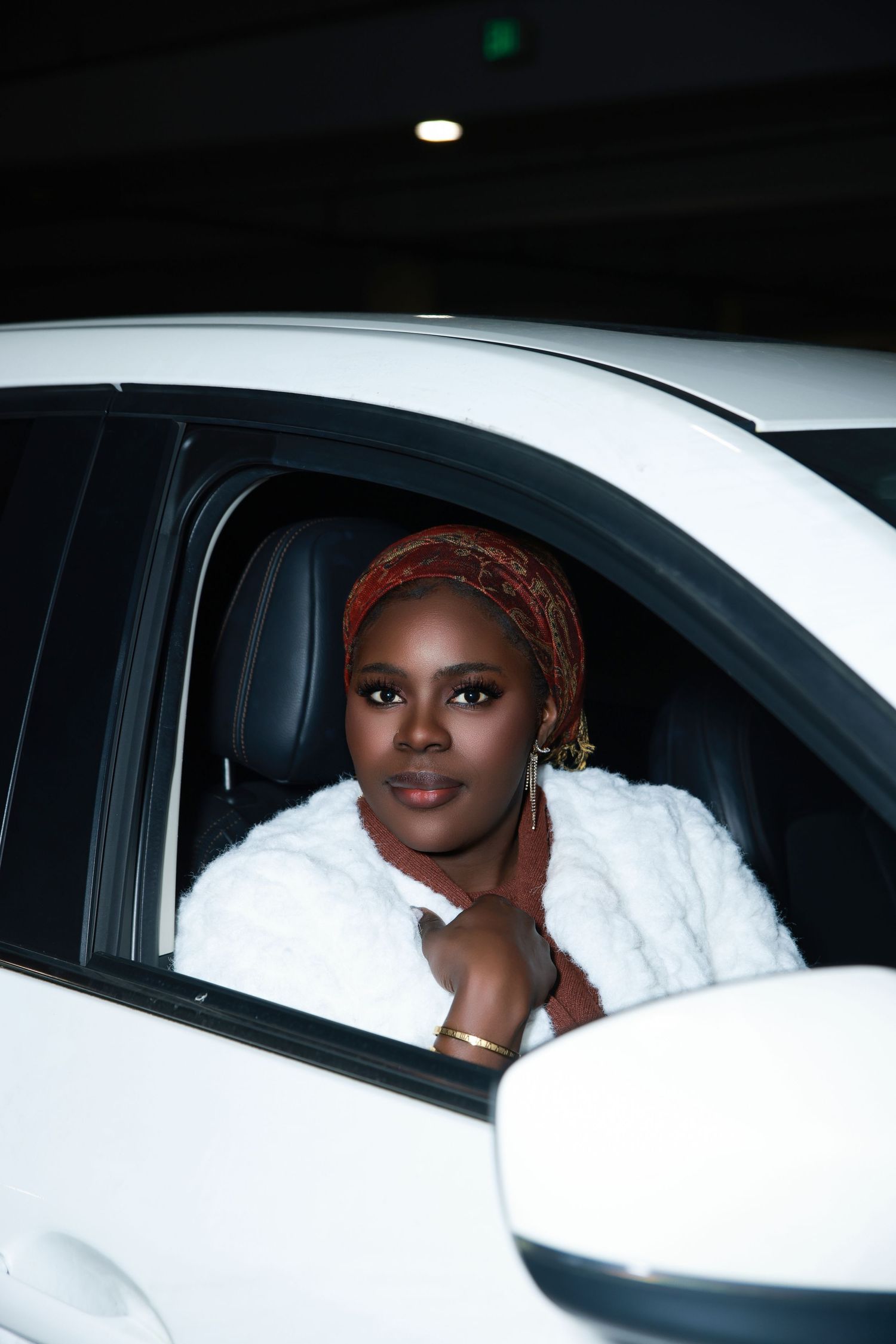 Bride in white dress and headscarf sitting in car window during wedding day.