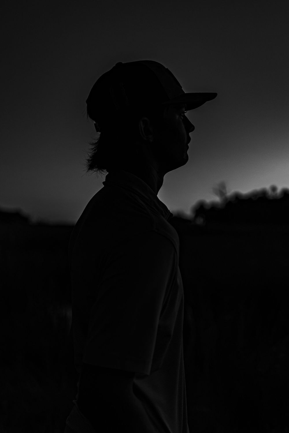 Silhouette of a young man wearing a baseball cap against a dark twilight sky for his senior portraits in Chiefland, FL