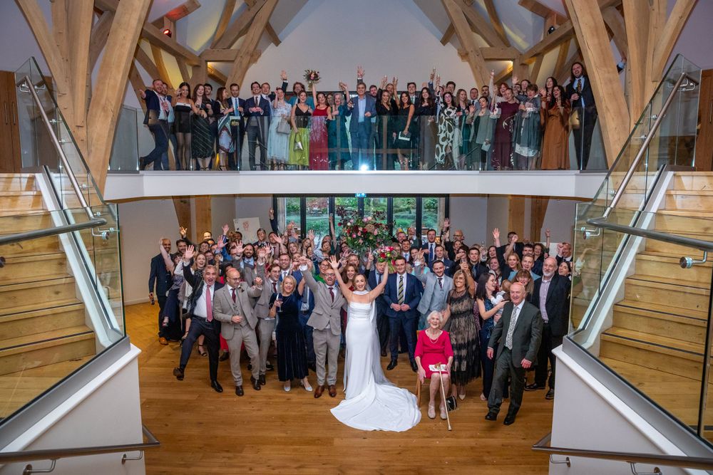 Large wedding party group photo taken from above in a stunning oak barn venue.