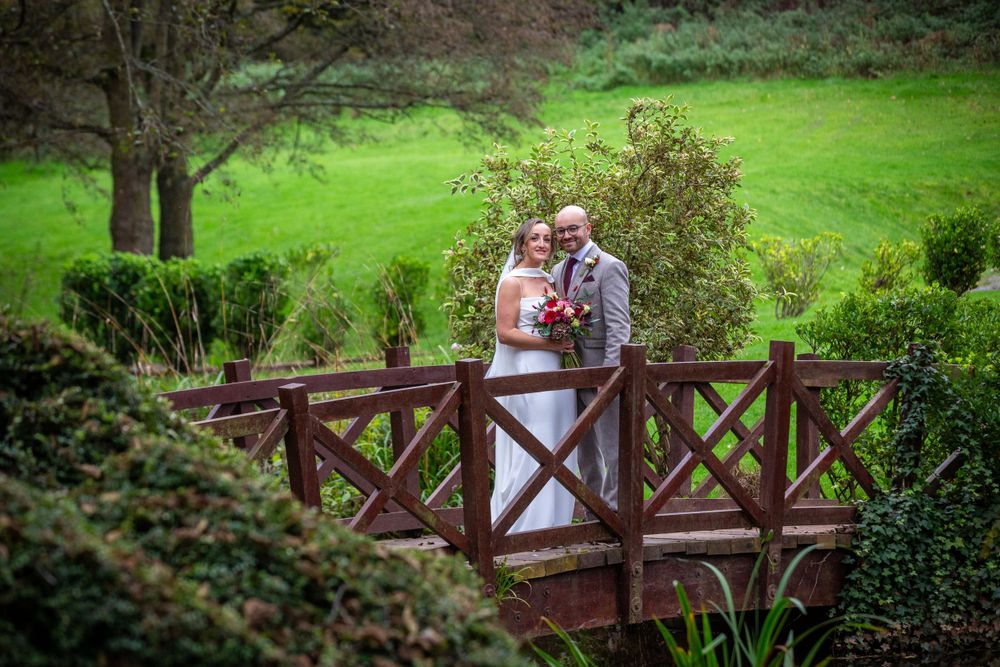 Bride and groom share a romantic moment on a wooden bridge surrounded by lush greenery.