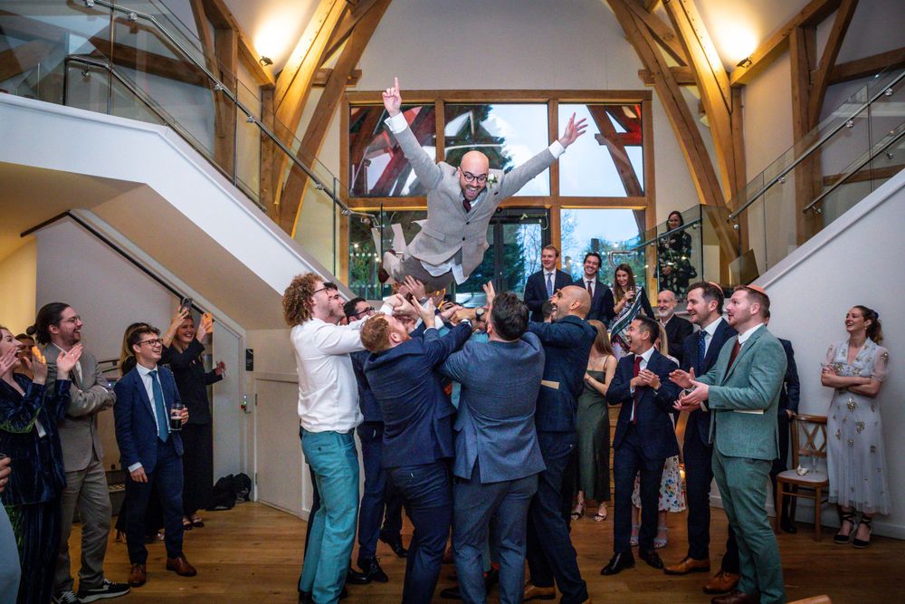 Groom is lifted and tossed in the air by groomsmen during joyful wedding celebration.