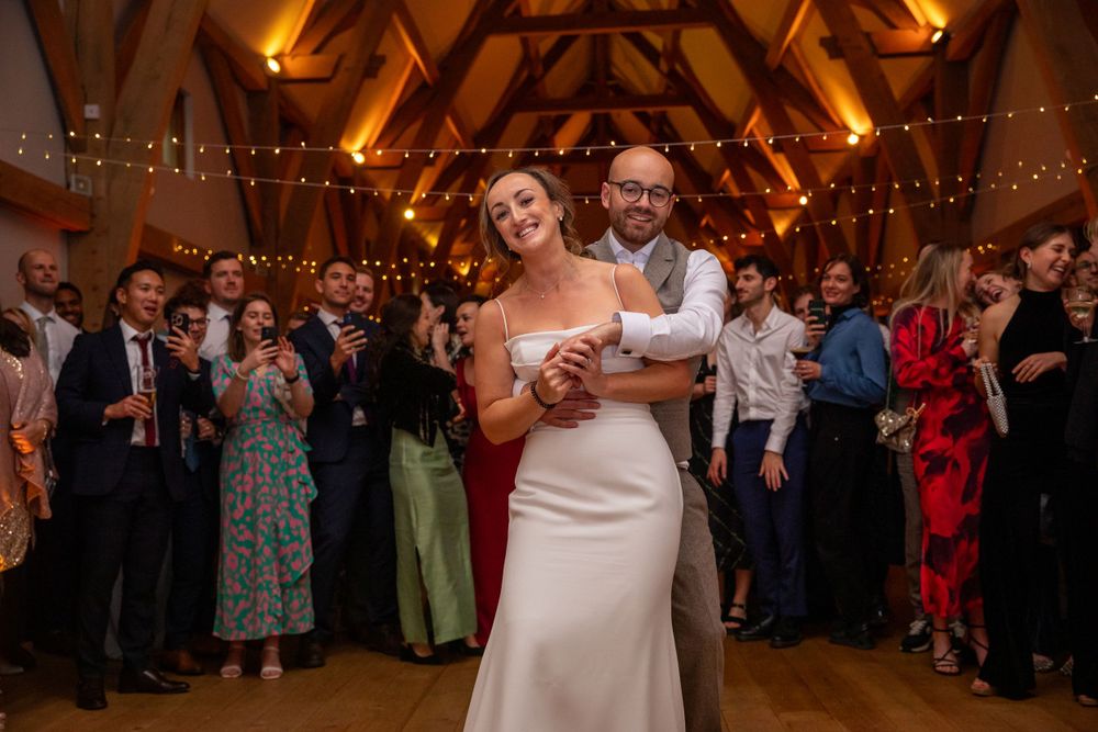 Bride and groom share their first dance in a warmly lit barn with fairy lights.