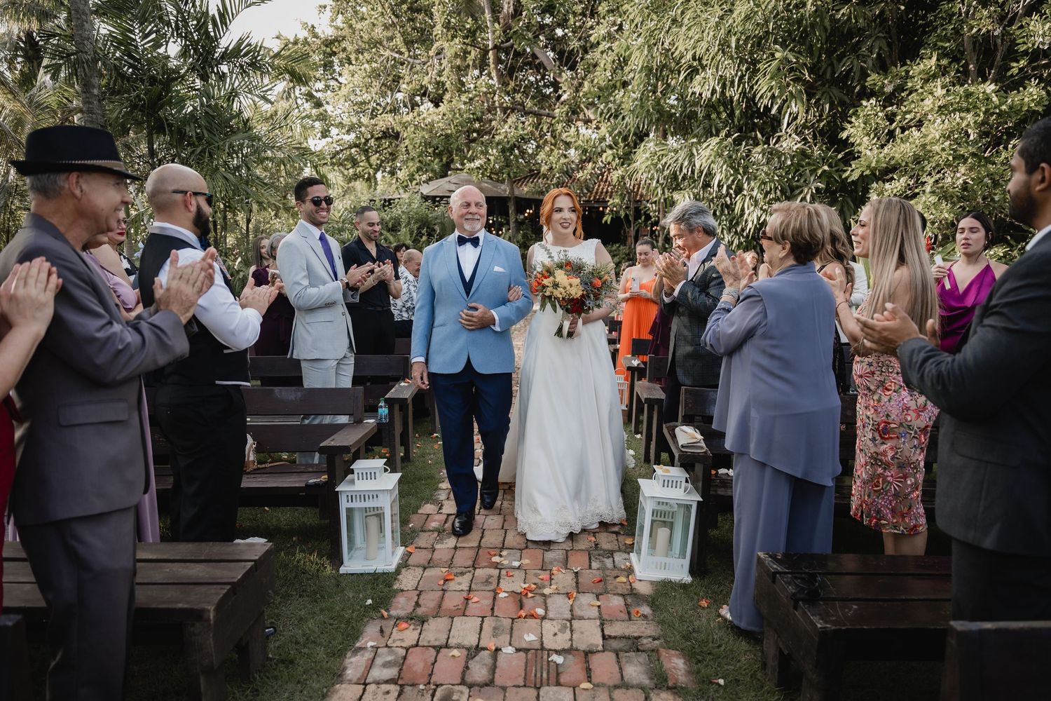 Outdoor wedding ceremony on brick pathway with wooden benches and lanterns at rustic venue.