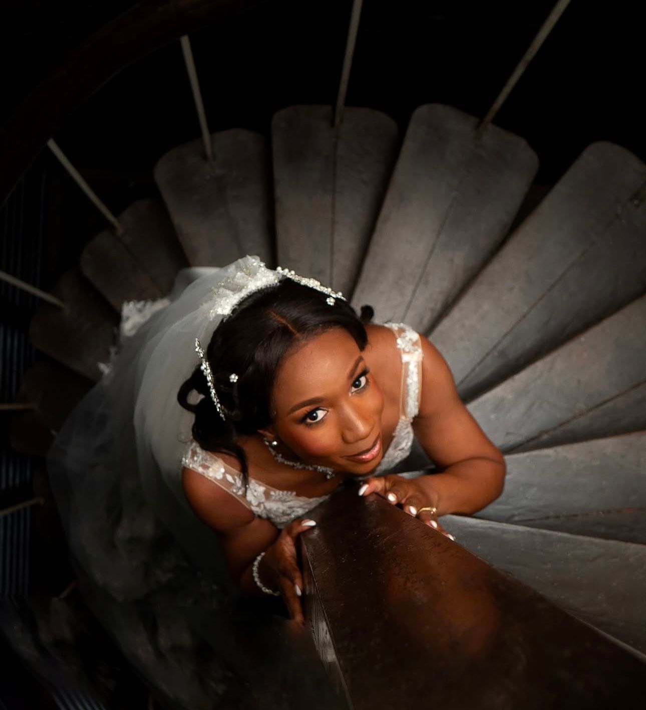Dramatic overhead shot of bride on spiral staircase in elegant lace wedding gown.