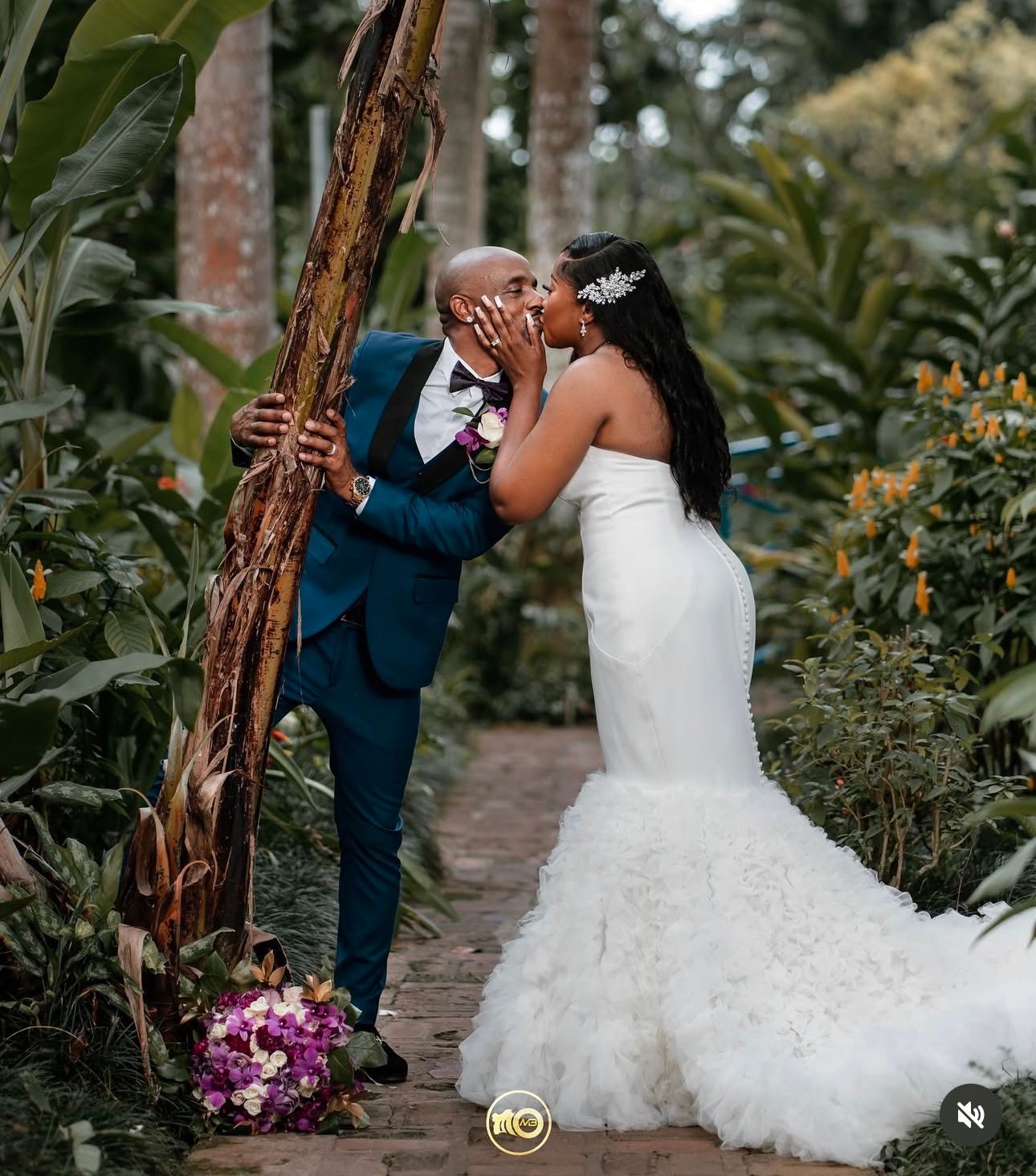 Wedding couple shares intimate moment in lush garden setting with purple bouquet.