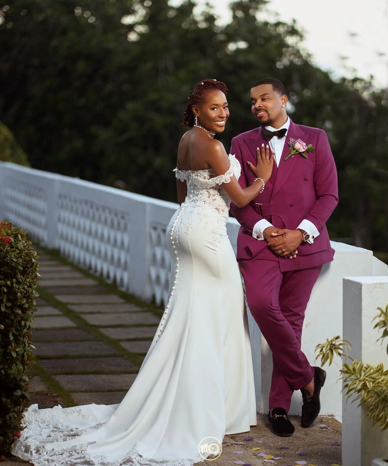 Wedding couple shares tender moment on white fence pathway.