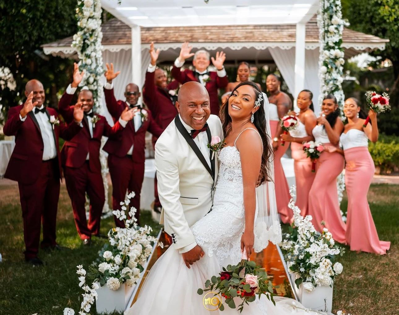 Wedding party poses under white arch with pink and burgundy color scheme.