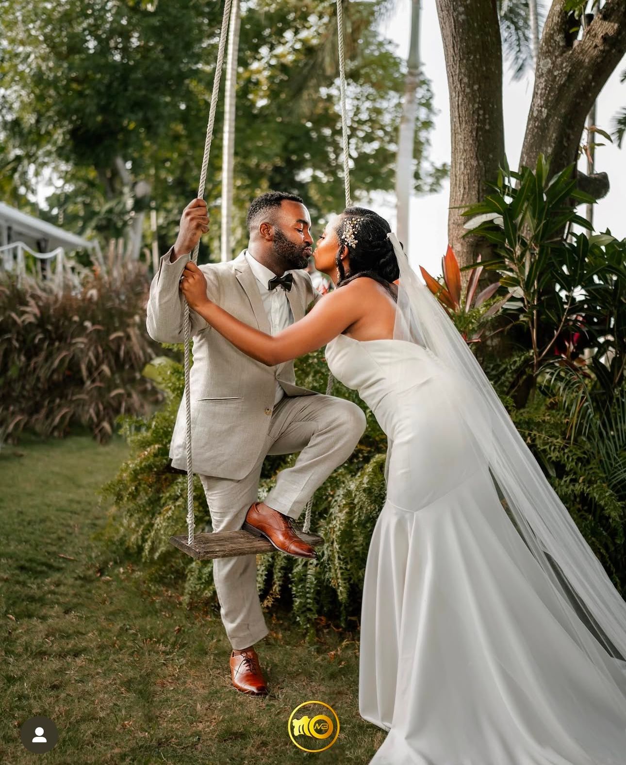 Playful wedding couple dances under trees in outdoor garden setting.