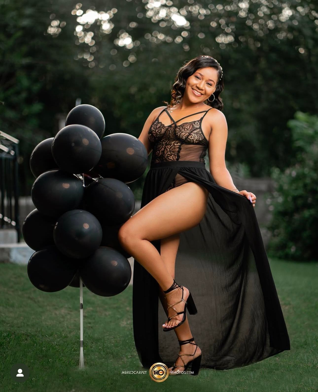 Elegant portrait session with black balloons and flowing black dress in an outdoor garden setting.