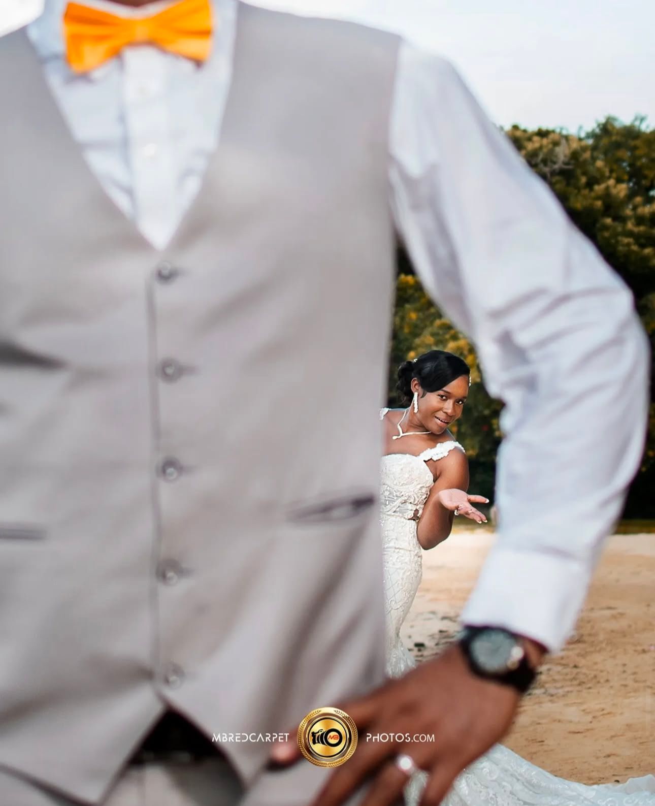 Wedding party members in gray suits with bright orange bowties pose together on a sunny day.