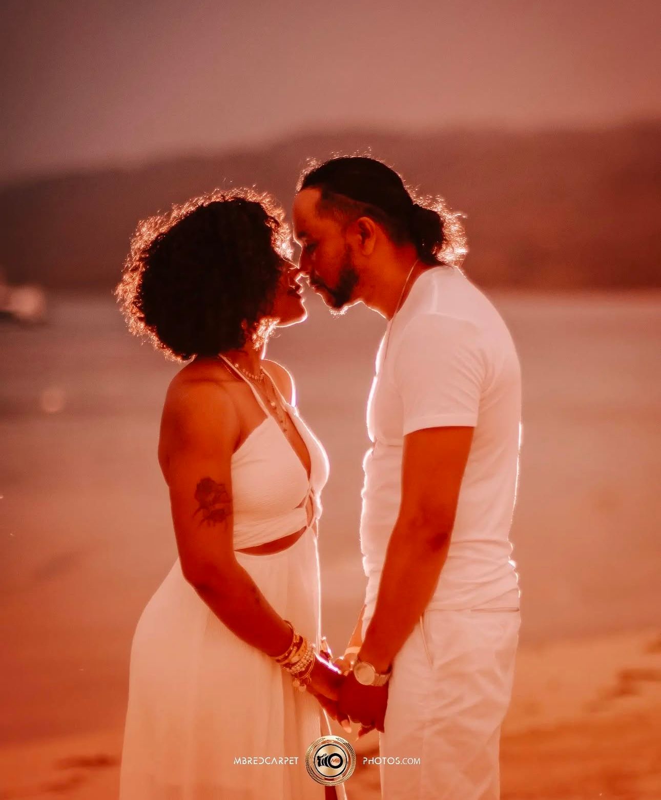 Romantic couple embraces during sunset photoshoot with warm orange lighting on the beach.