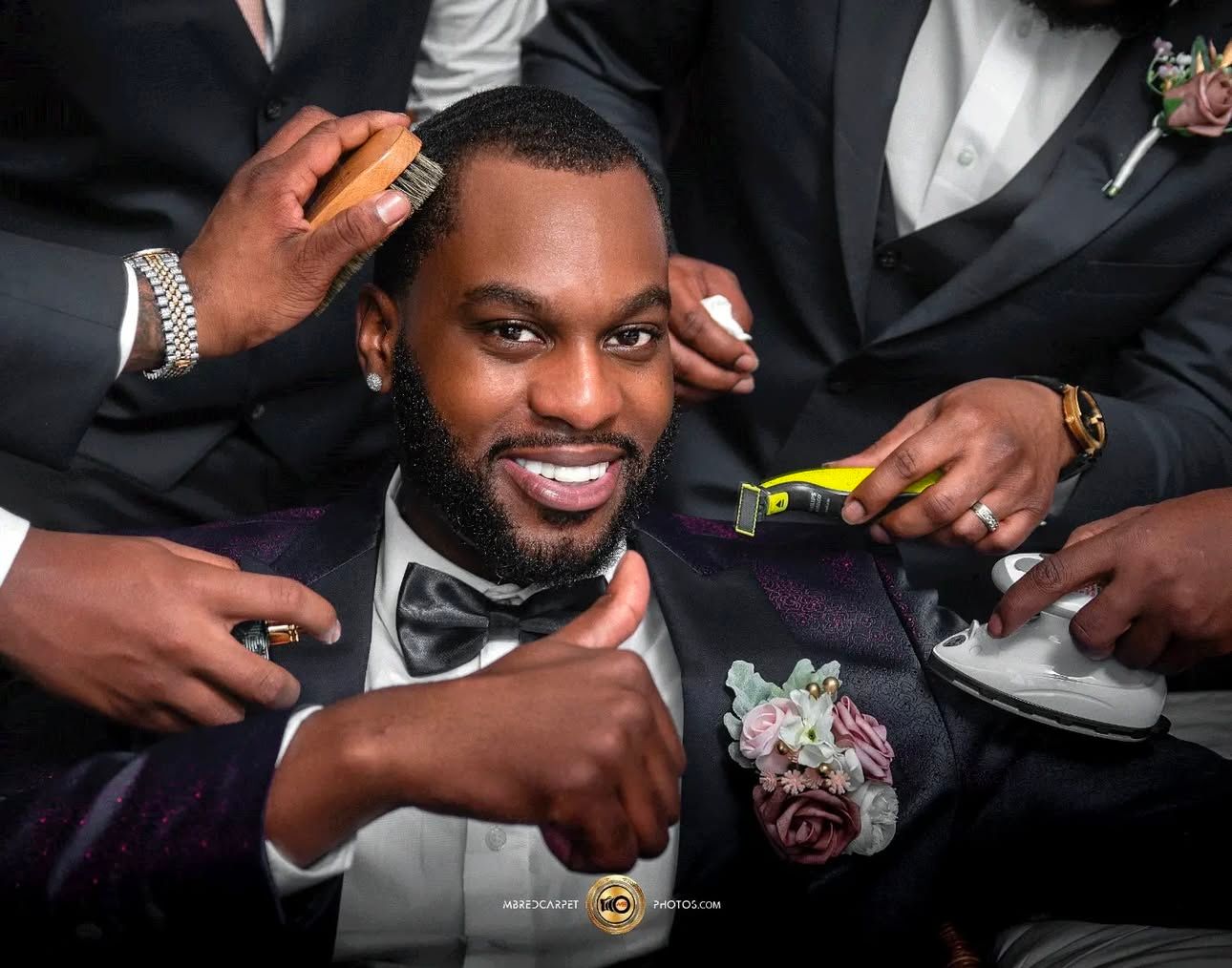 Groomsmen share laughs while getting ready in formal black tuxedos.
